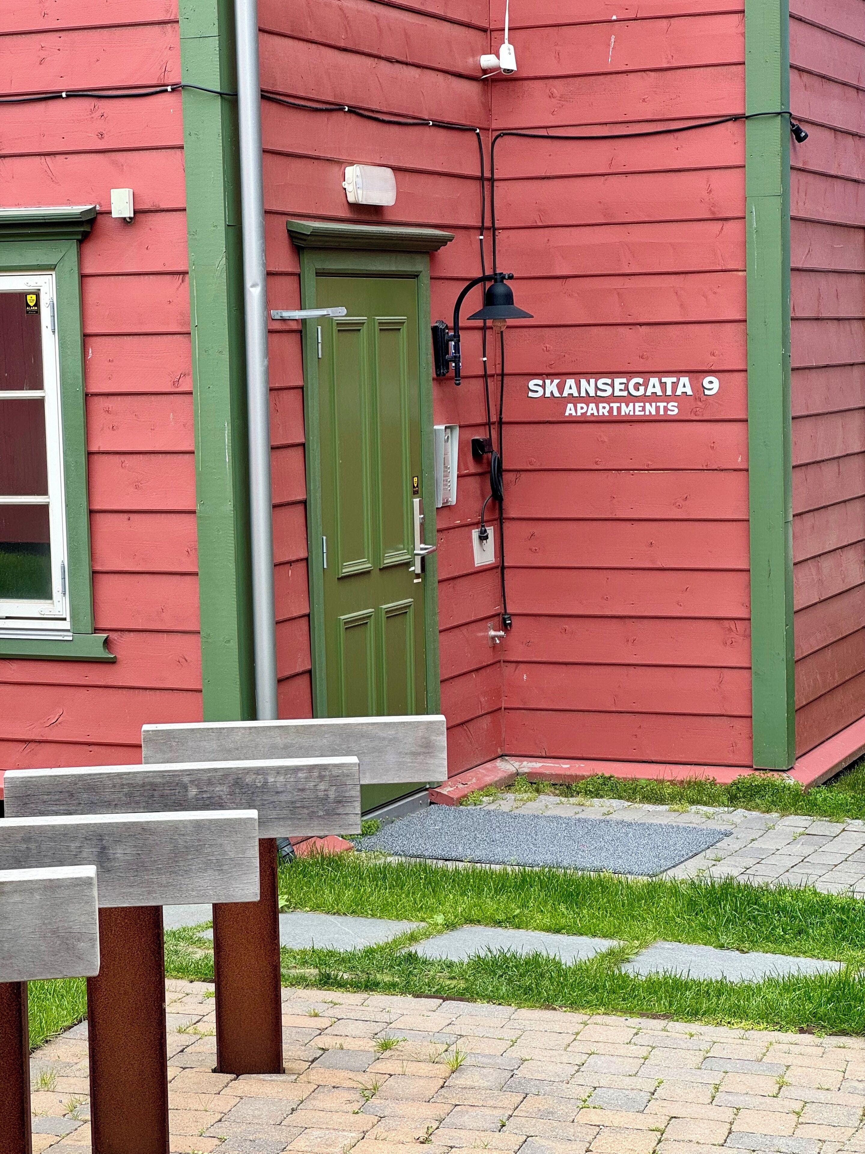 Ein rotes Gebäude mit einer grünen Tür und einem Schild, auf dem 'SKANSEGATA 9 APARTMENTS' steht.