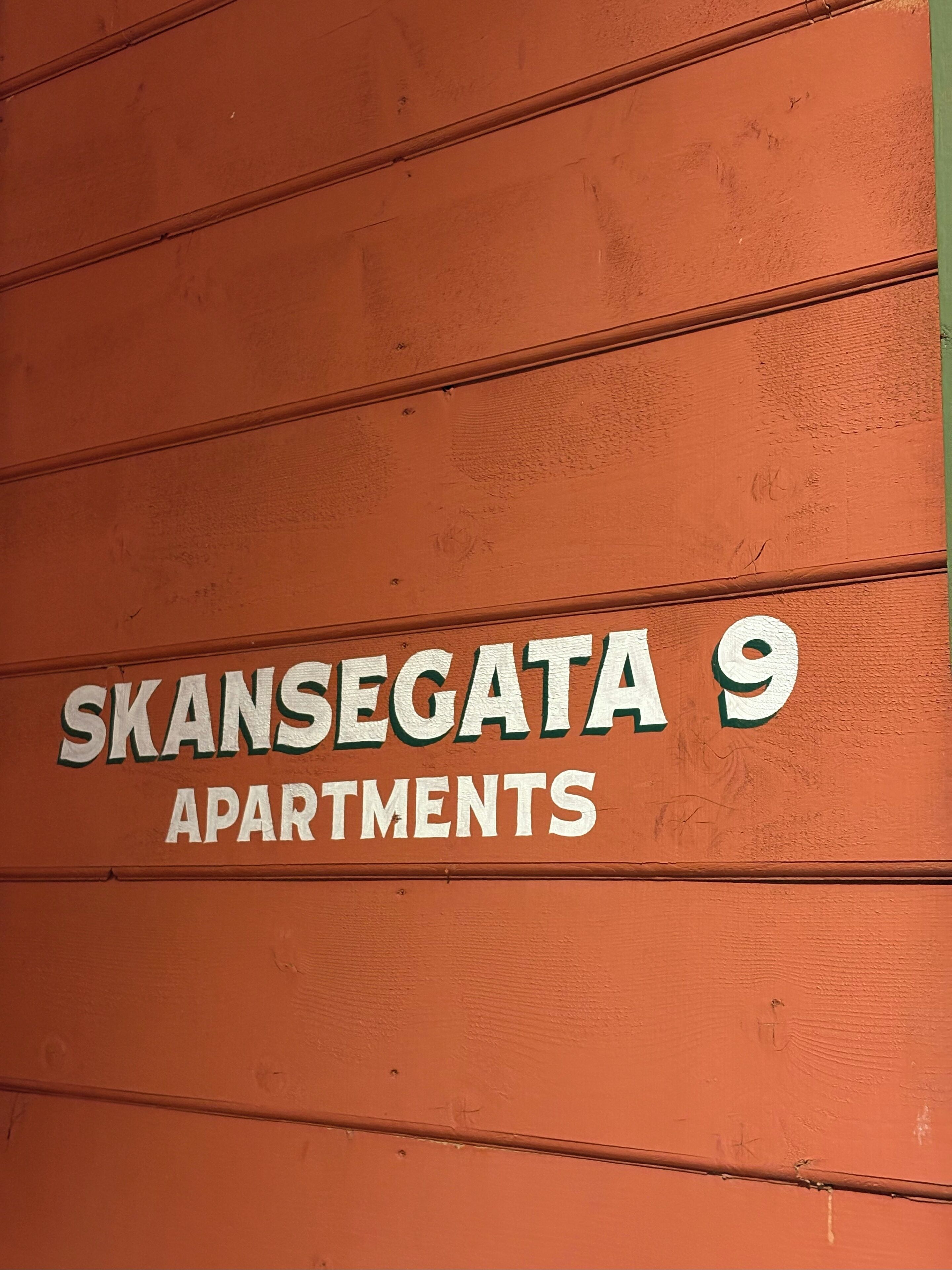 A sign for "SKANSEGATA 9 APARTMENTS" on a textured orange wall.