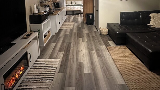 Un salon chaleureux avec une cheminée, un canapé en cuir noir, un téléviseur et un plancher en bois.