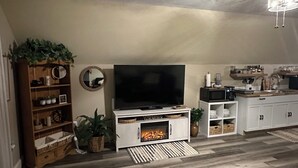 Un salon avec une cheminée, un téléviseur, des étagères en bois et un coin cuisine.