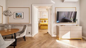 Een moderne woonkamer met een eethoek, een televisie en een bed met een gele hoofdeinde.