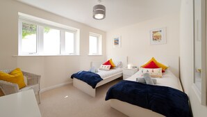 A bedroom with two beds, a white chair, and a small table. - Dog friendly, two bedroom holiday apartment with balcony in Mortehoe, North Devon. (Mortehoe)