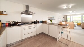 A modern kitchen with a central island, stainless steel appliances, and a large window providing natural light. - Dog friendly, two bedroom holiday apartment with balcony in Mortehoe, North Devon. (Mortehoe)