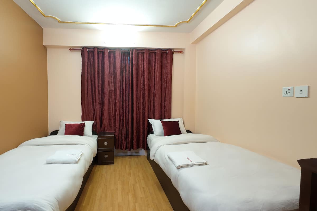 A hotel room with two single beds, a nightstand, a lamp, and a curtain.