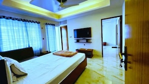 Une chambre d’hôtel avec un lit, un téléviseur fixé au mur, une porte en bois et un ventilateur de plafond.