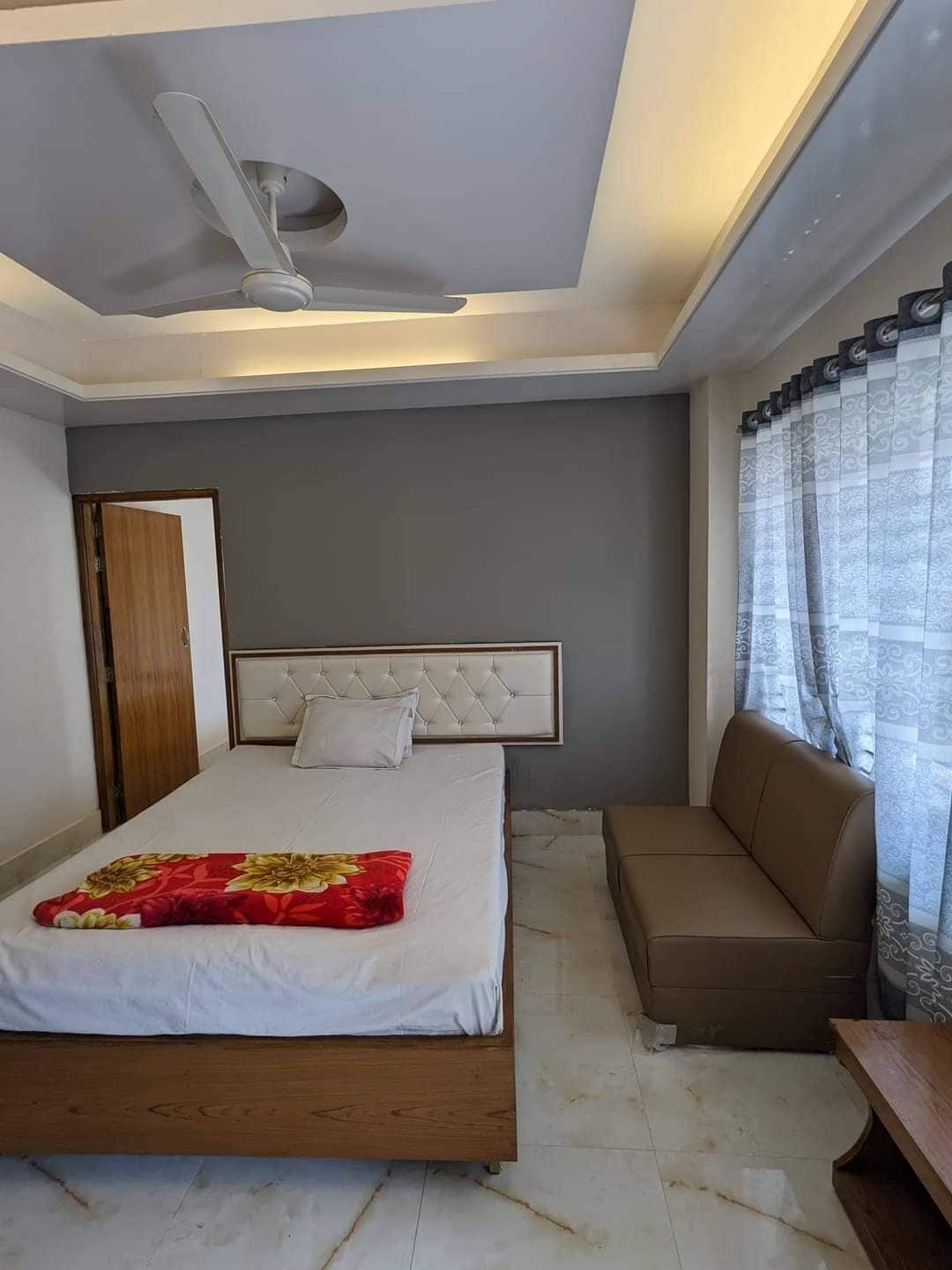 A bedroom with a bed, a sofa, a ceiling fan, and a window with curtains.
