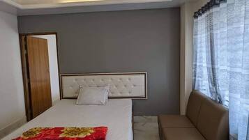 A bedroom with a bed, a sofa, a ceiling fan, and a window with curtains.
