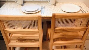 Una mesa de comedor con dos sillas, una ventana con persianas y vistas a la vegetación.