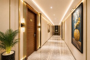 A hotel hallway with a marble floor, wooden doors, and a potted plant. - Hotel Le Premier (New Delhi)