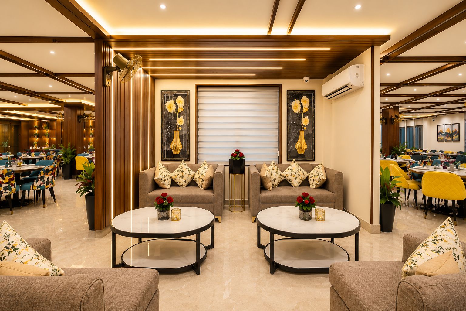 A hotel lobby with a seating area featuring sofas and round tables, a large window with blinds, and a ceiling with wooden beams and recessed lighting.