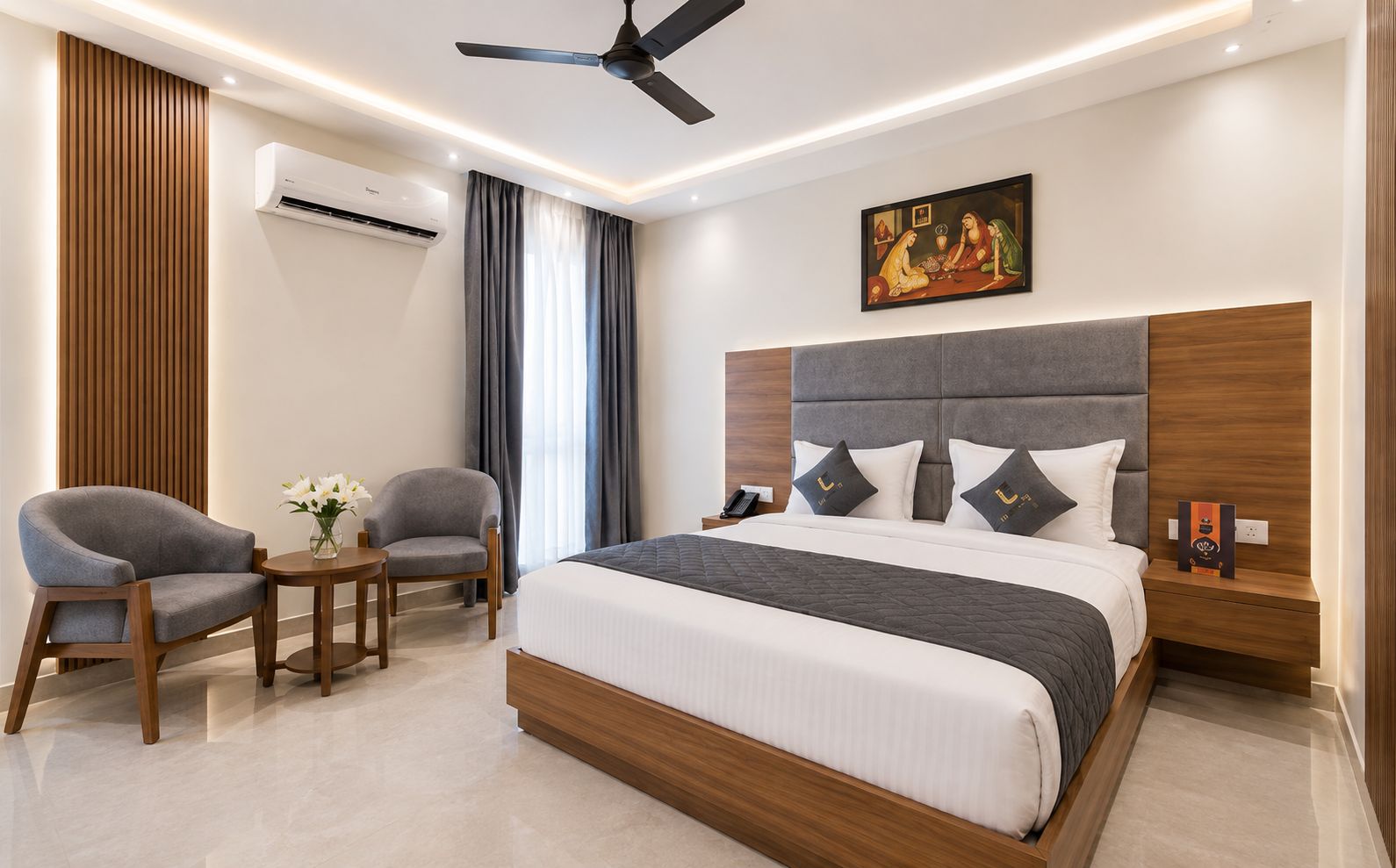 A modern hotel room with a large bed, two armchairs, a small table, an air conditioning unit, a ceiling fan, and a painting on the wall.