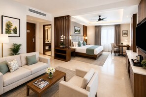 A hotel room with a sofa, a coffee table, a bed, a desk, and a TV. - Hotel Le Premier (New Delhi)