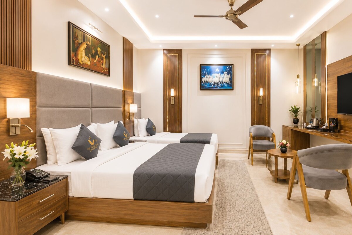 A hotel room with a bed, bedside tables, a desk, a chair, a TV, and artwork on the walls.
