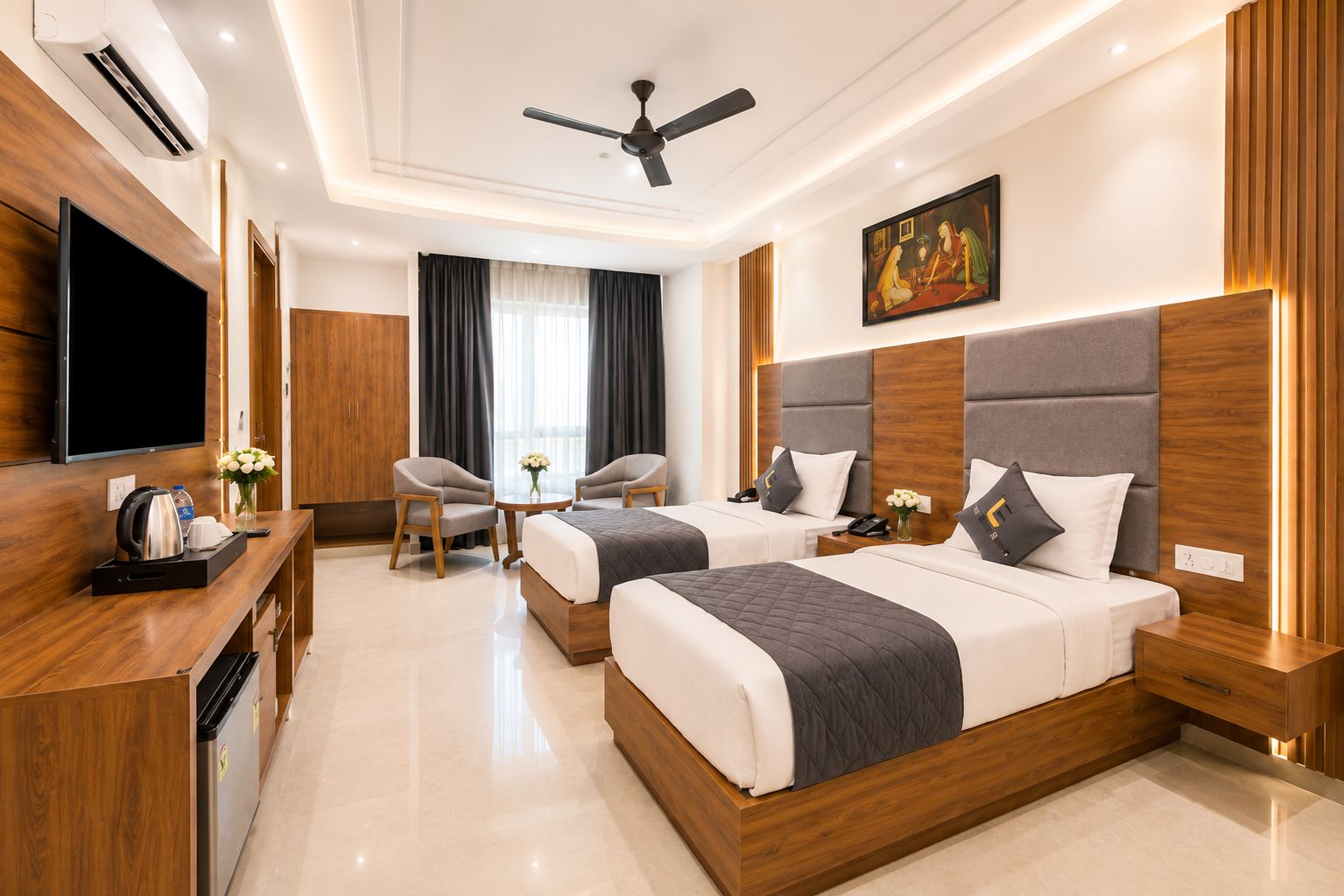 A hotel room with two beds, a desk, a TV, and a ceiling fan.