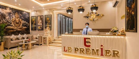 Zona de recepción de un hotel con mostrador, una estatua de Buda y un mural grande.