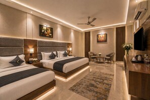 A hotel room with two beds, a desk, a chair, a TV, and artwork on the walls. - Hotel Le Premier (New Delhi)