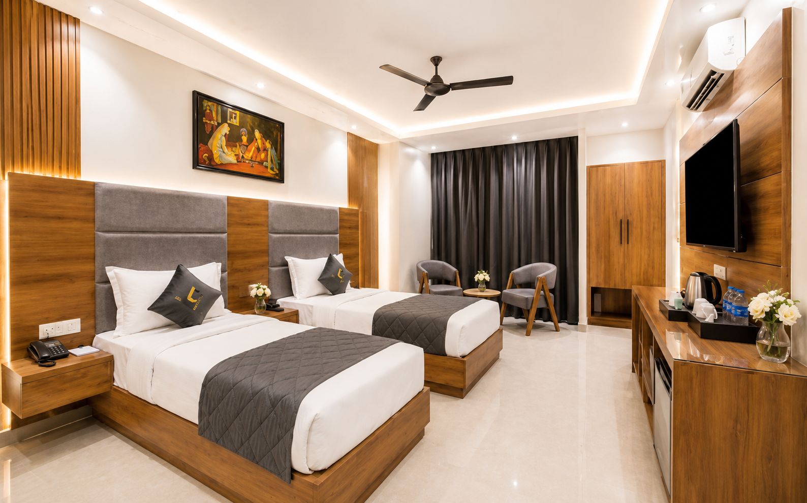 A hotel room with two beds, a ceiling fan, a TV, a desk with a coffee maker, and a painting on the wall.