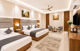 A hotel room with two beds, a desk, a chair, a TV, and artwork on the walls.