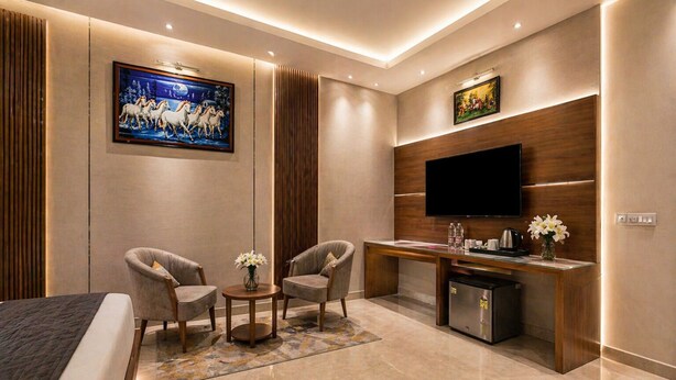 Une chambre d’hôtel moderne équipée d’un lit, de deux fauteuils, d’une petite table avec des fleurs, d’un bureau avec une télévision et d’un mini-bar.