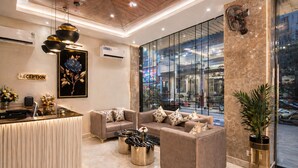 A modern reception area with a reception desk, sofas, a coffee table, and a large window offering a view of the street. - Hotel Le Premier (New Delhi)