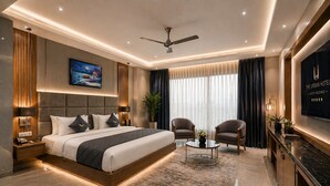 A modern hotel room with a large bed, a ceiling fan, a flat-screen TV, and a seating area with two armchairs and a coffee table. - Hotel Le Premier (New Delhi)