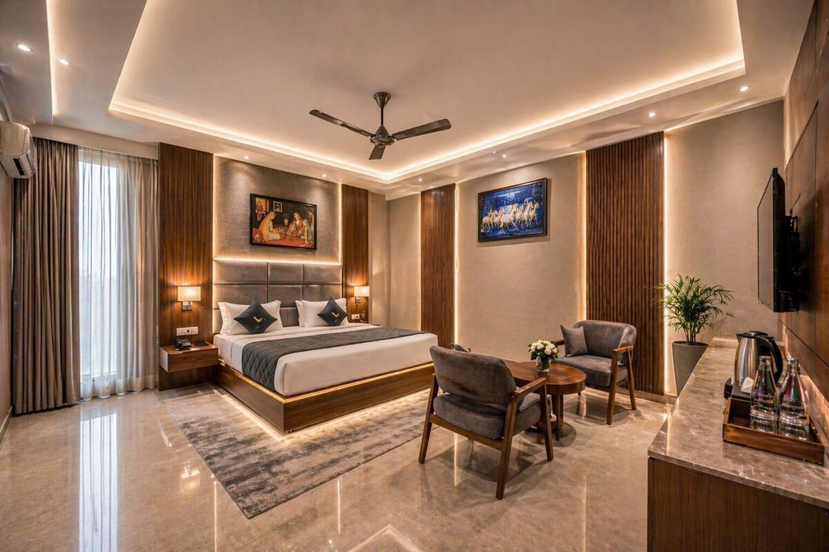 A modern hotel room with a large bed, a desk, two armchairs, a ceiling fan, and a TV.