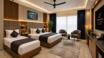 Habitación de hotel con dos camas, zona de estar, televisor y vistas a la ciudad.