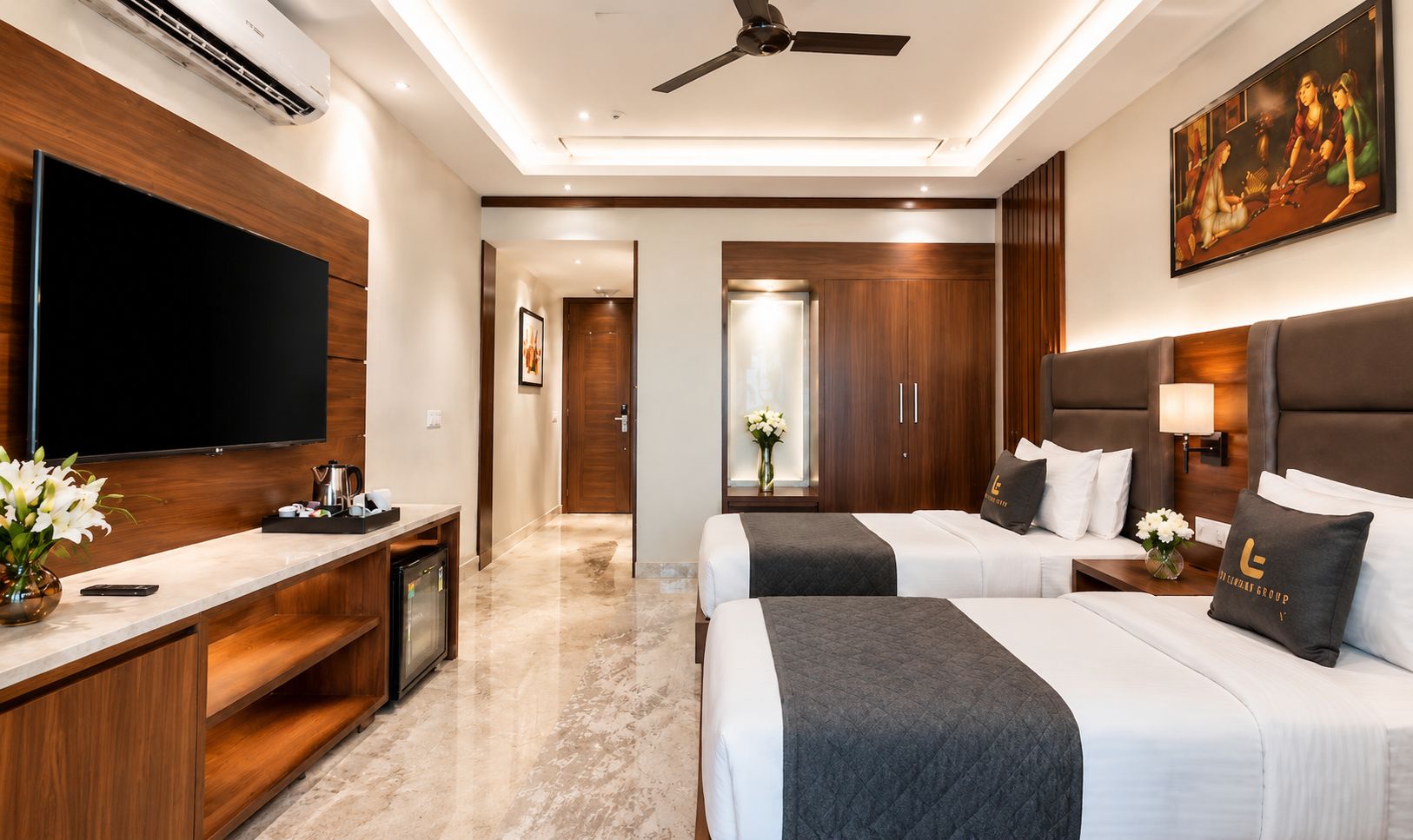 A hotel room with a flat-screen TV, a desk with a coffee maker, two beds with headboards, a painting on the wall, and a ceiling fan.