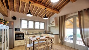 A kitchen with wooden beams, a dining table with chairs, a refrigerator, an oven, and a window with curtains.