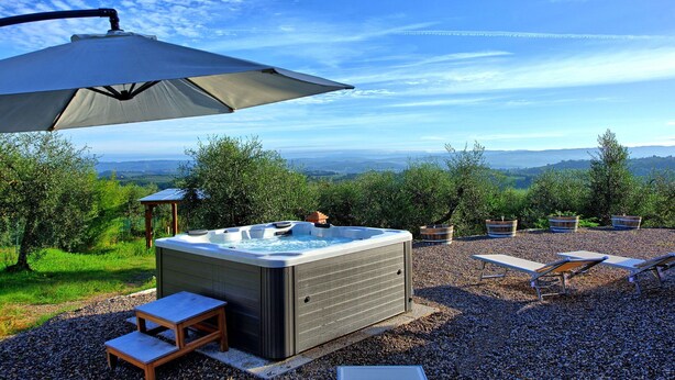A hot tub with a view of rolling hills, surrounded by a gravel patio with lounge chairs and a pergola providing shade.