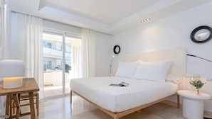 Ein modernes Hotelzimmer mit einem großen Bett, einem Nachttisch mit Lampe und Blick auf den Außenbalkon.