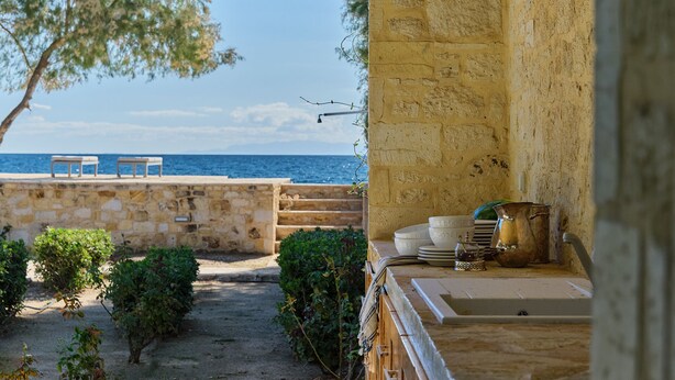 A stone building with a view of the sea, outdoor seating, and a table with dishes and a kettle. - Villa Plomari On The Sea- Entire House or Split Villa (Agios Isidoros)