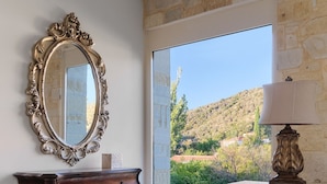 A room with a large mirror, wooden dresser, and a lamp. There is a view of a hillside through a glass door. - Villa Plomari On The Sea- Entire House or Split Villa (Agios Isidoros)