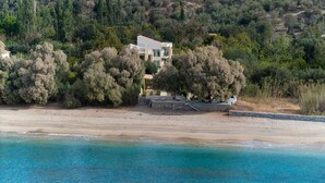 A coastal property with a modern house surrounded by dense trees, a beach, and a clear blue sea. - Villa Plomari On The Sea- Entire House or Split Villa (Agios Isidoros)