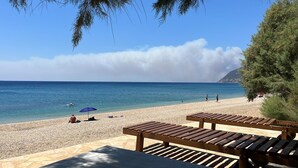 A beach with wooden loungers and a blue umbrella. - Villa Plomari On The Sea- Entire House or Split Villa (Agios Isidoros)