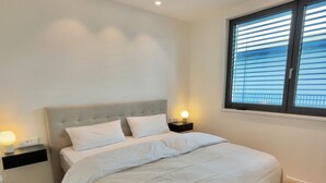 A bedroom with a large bed, two bedside tables with lamps, a window with blinds, and a ceiling with recessed lighting. - Beautiful apartment in historic Wangen im Allgäu (Wangen im Allgäu)