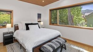 A bedroom with a large window, a bed with white bedding, a nightstand, and a patterned rug. - Rio Vista Telluride w/ hot tub! (San Miguel County)