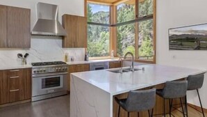 A modern kitchen with a large island, wooden cabinets, and a view of the outdoors. - Rio Vista Telluride w/ hot tub! (San Miguel County)