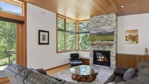A living room with a stone fireplace, leather sofas, and large windows offering a view of the outdoors. - Rio Vista Telluride w/ hot tub! (San Miguel County)