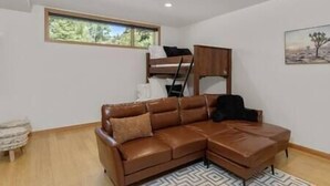 A modern room with a brown leather sofa, a bunk bed, and a window with a view of trees. - Rio Vista Telluride w/ hot tub! (San Miguel County)