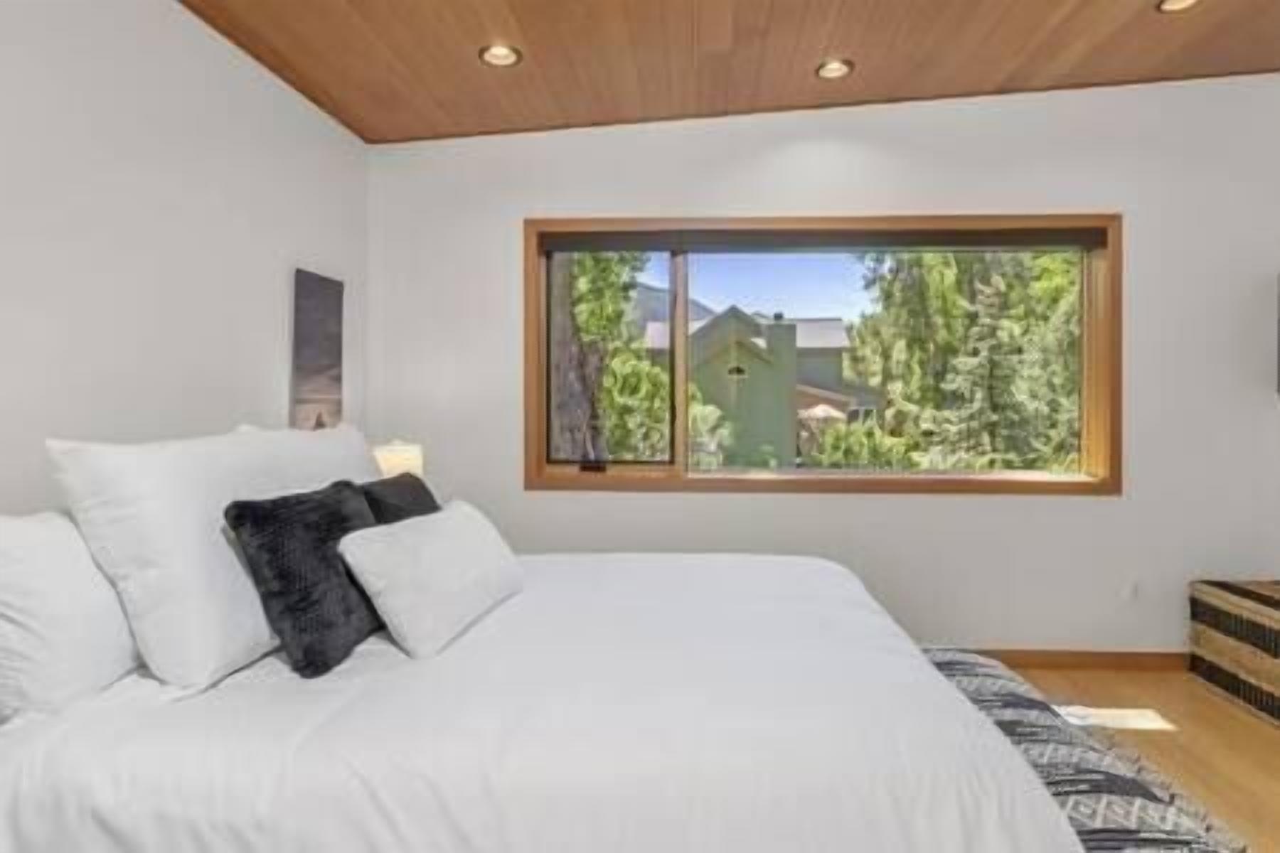 Ein Schlafzimmer mit einem großen Bett, einem Fenster mit Blick auf Bäume und ein Haus, sowie einer Holzbalkendecke.