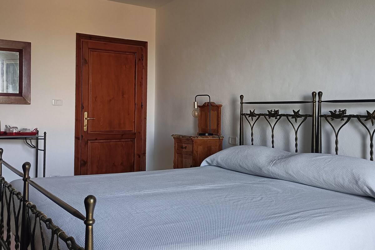 A bedroom with a bed, wooden wardrobe, and a desk with a mirror.