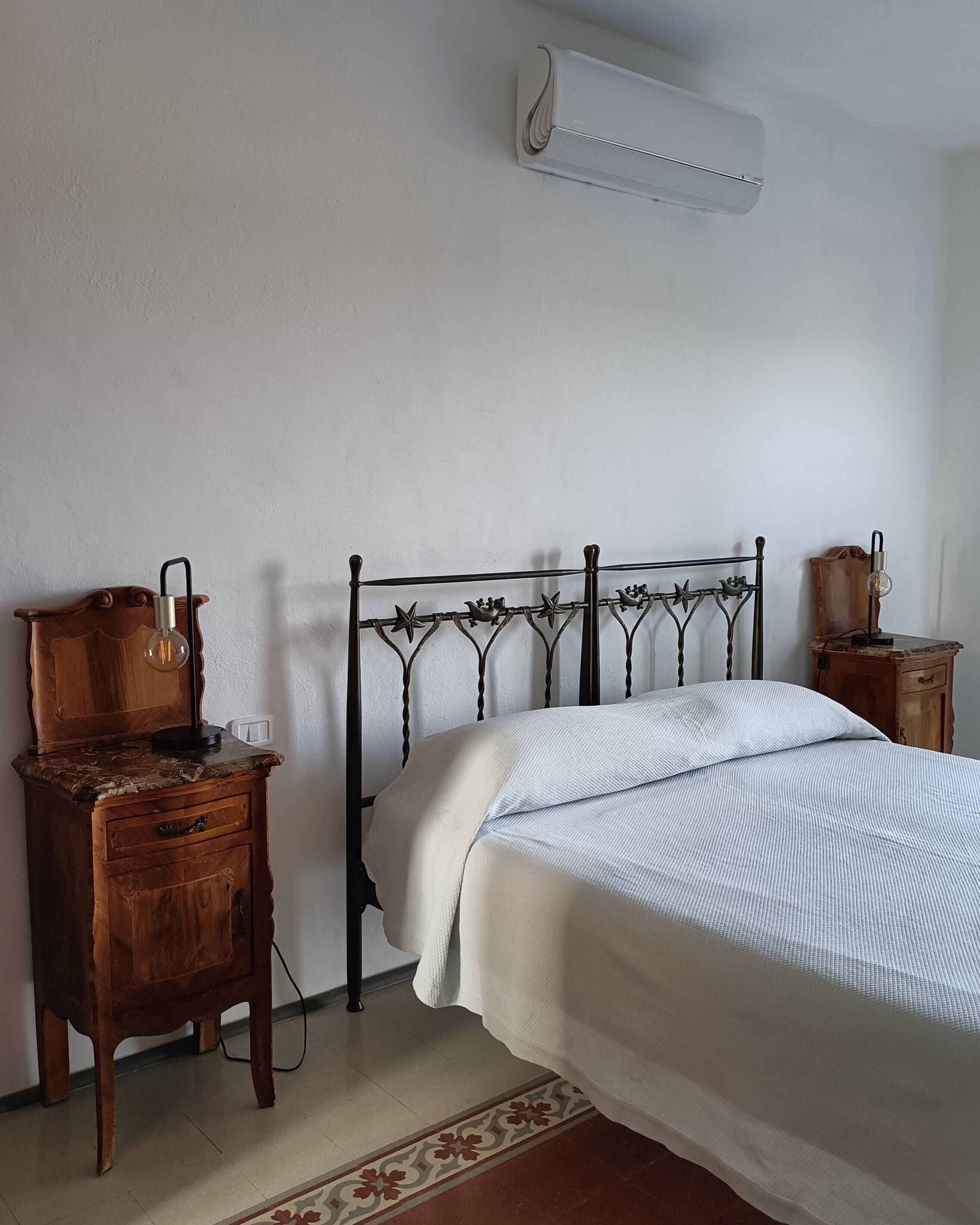 A bedroom with a metal bed frame, a wooden nightstand, a bedside table, and a wall-mounted air conditioner.