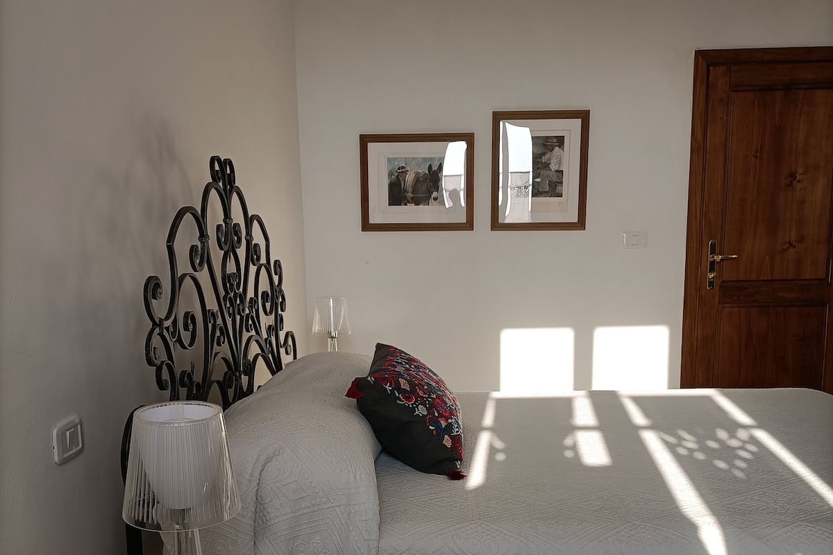 A bedroom with a bed, a bedside table with a lamp, a mirror, and a door.