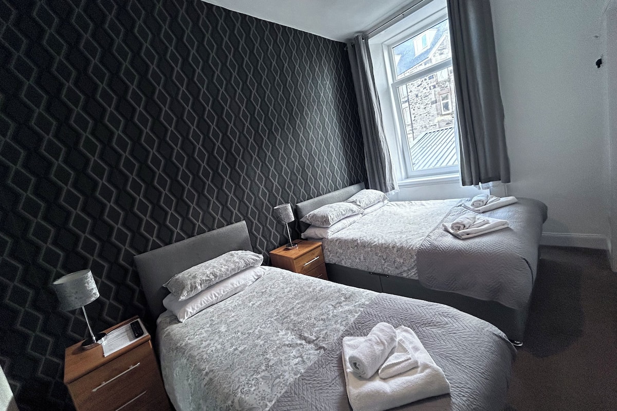 Une chambre d’hôtel avec deux lits, une table de chevet, une lampe et une fenêtre avec des rideaux.