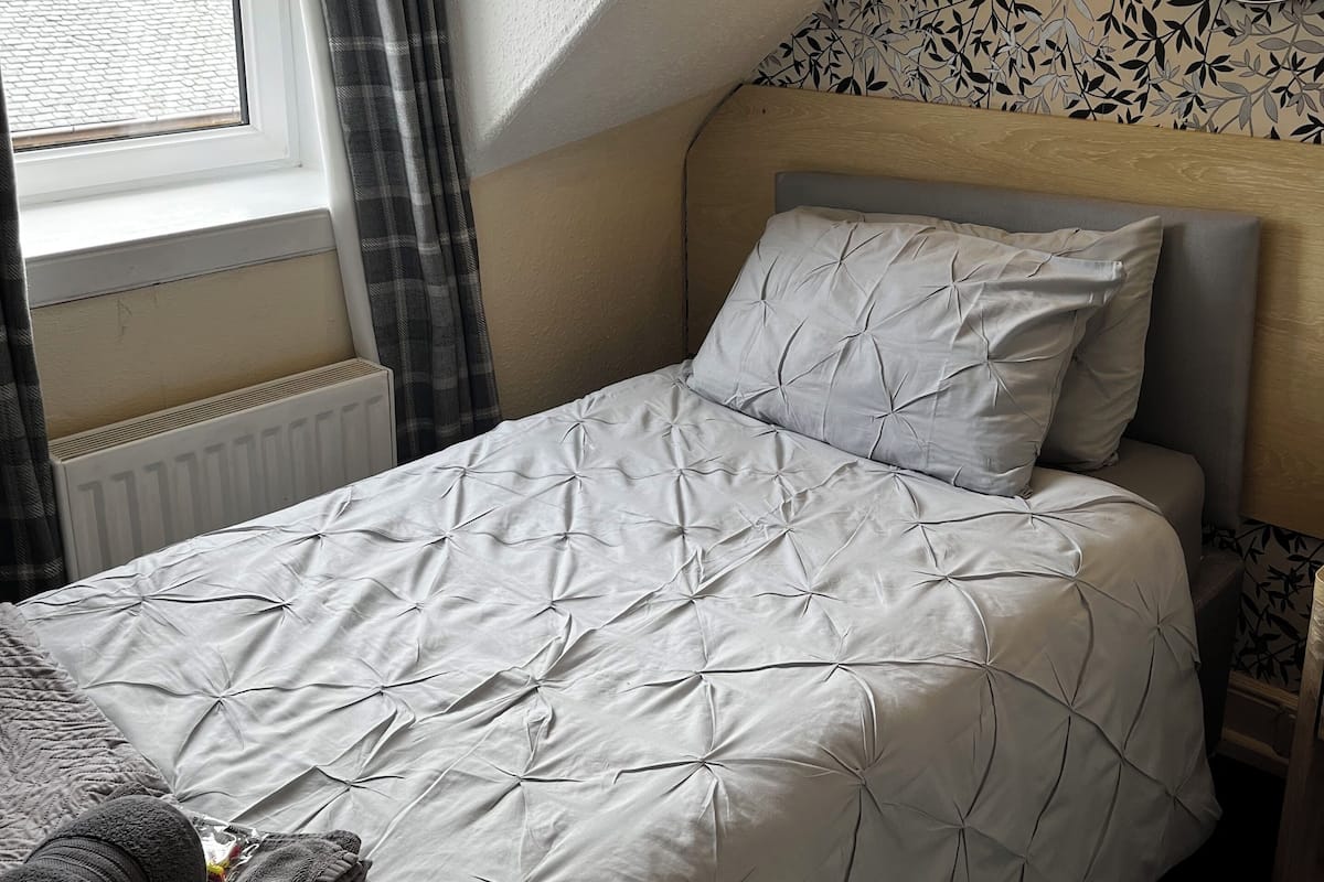 Un lit bien fait, avec une couette à motifs géométriques, une lampe de chevet et une fenêtre avec des rideaux.
