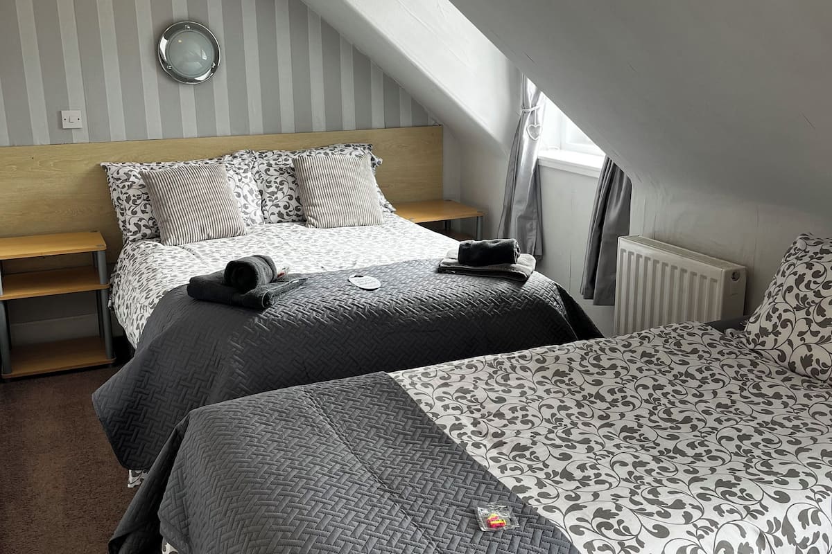 Une chambre avec deux lits, une tête de lit en bois, une table de chevet, un radiateur et un puits de lumière.