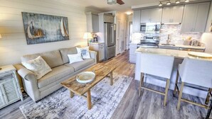 A modern kitchen with a central island, a dining area with a bar, and a living room with a sofa and coffee table. - Charming 1-bedroom condo in welcoming Isle of Palms with AC, WiFi (Isle of Palms)