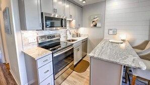 A modern kitchen with stainless steel appliances, grey cabinets, and a marble countertop. - Charming 1-bedroom condo in welcoming Isle of Palms with AC, WiFi (Isle of Palms)