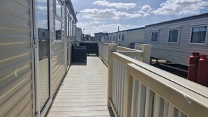 A corridor with mobile homes, a wooden deck, and a railing. - 3-bed Caravan, Sleeps 8, Pool & Beach (Skegness)